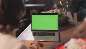 Family couple at home near glowing Christmas tree spend time together celebrate Christmas and look at green screen copy space chroma key laptop. New Year celebration, gifts purchase online concept