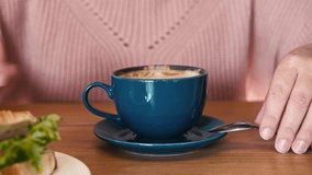 Unrecognizable woman wearing warm cosy pink sweater is drinking coffee with croissant in a cafe. Female person sitting and drinking cappuccino from blue ceramic mug. Hands with Cup close up, Cropped. - Powered by Shutterstock - Get 15% off with code: PIKWIZARD15
