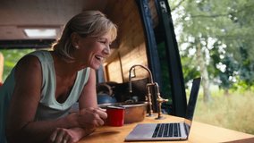 Senior retired woman on camping trip in countryside inside RV using laptop to make video call - shot in slow motion