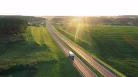 Long haul semi truck driving on intercity highway in rural region at sunset sun shines. Agricultural green crop fields and hills in background. Stage of delivery and logistics goods, aerial motion - Powered by Shutterstock - Get 15% off with code: PIKWIZARD15