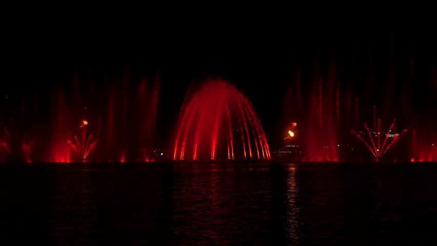 A beautiful fire show and a show of colorful fountains on a small lake. Flashes of fire and jets of water in the dark.