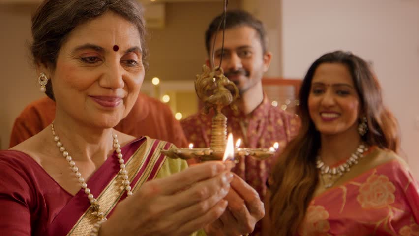 Happy smiling Hindu ethnic Indian family group members lighting up traditional diyas or oil lamps on the Religious occasion of Diwali festival in decorated house. Festive season, relationship concept. Royalty-Free Stock Footage #1109794877