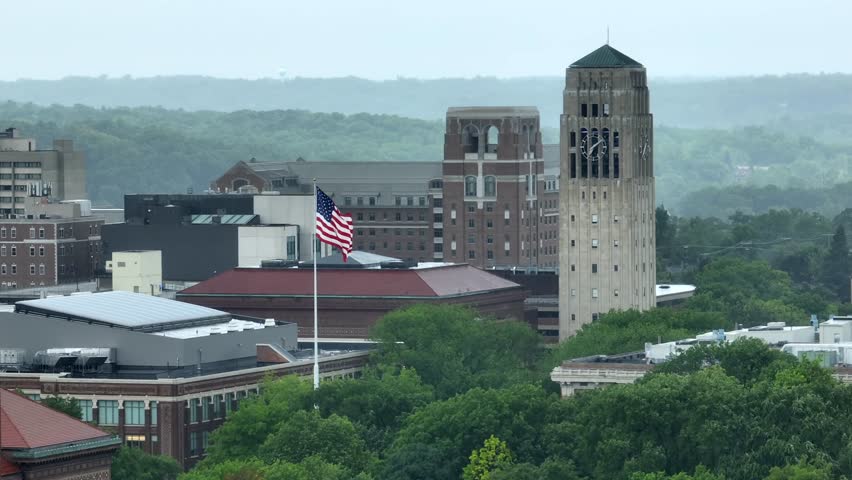 American flag waving beside University of Michigan clock tower, Burton Memorial Tower. Aerial establishing shot.