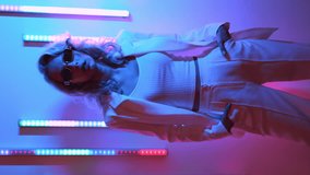 Vertical video. Young beautiful hipster woman in street style fashion concept. Hot model wearing white suit and sunglasses. Female posing in blue neon light in studio interior - Powered by Shutterstock - Get 15% off with code: PIKWIZARD15