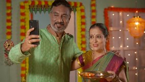 elderly Indian couples making video call on mobile phone during diwali festival celebration at home - concept of distance relations, technology and traditional culture