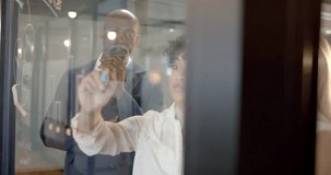 Vertical video of diverse business people by glass wall in office with copy space. Business, work, office, professionals and teamwork concept, unaltered.
