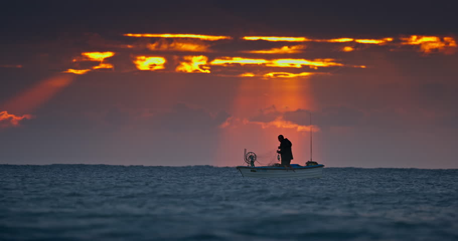 Fisherman and old wooden fishing boat silhouettes against beautiful sea horizon at sunrise dramatic landscape with sun rays though the clouds Royalty-Free Stock Footage #1109803835