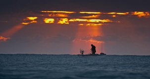 Fisherman and old wooden fishing boat silhouettes against beautiful sea horizon at sunrise dramatic landscape with sun rays though the clouds