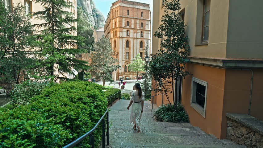 Beautiful tourist girl exploring Montserrat mountain village town by Barcelona. A female walking in Montserrat Monastery Resort with a mountain range in Catalonia, Spain.