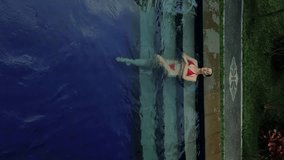 Vertical aerial video of a young woman in a red bikini lying in a swimming pool. A long-awaited vacation on the tropical island of Bali. Travel and peace concept. 