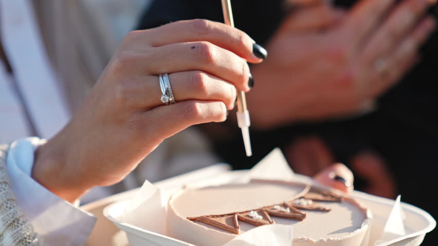 Female hand puts long single candle into the cake. Close up. Unrecognized male holding a baby at backdrop.