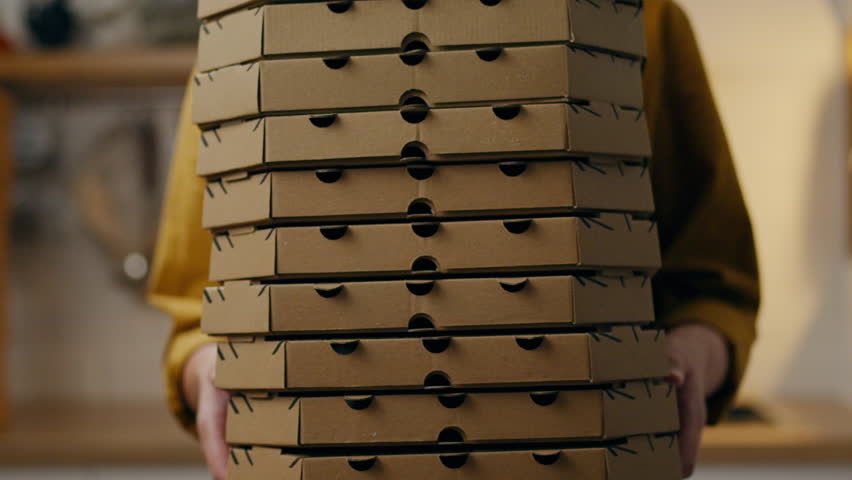 Small and medium business pizza baking shop, young employee baker holds a bunch of stack of cardboard boxes for pizza delivery. cardboard boxes for pizza in the hands of a food delivery courier