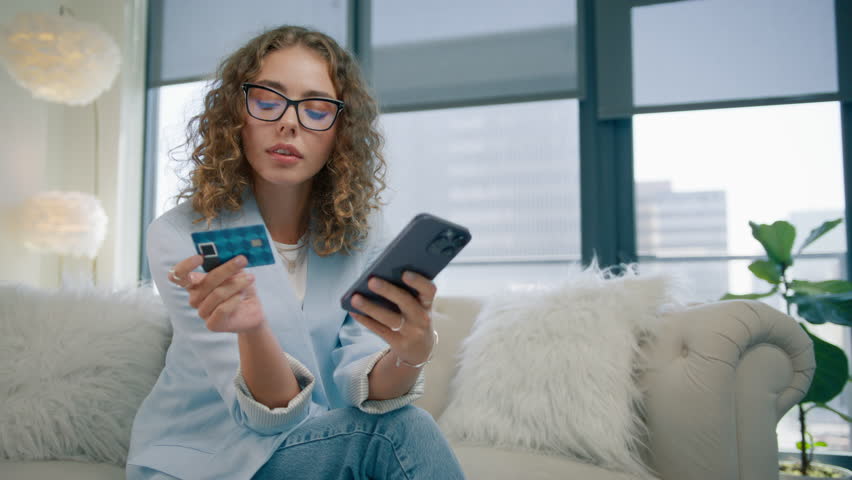 Smart stylish woman in protecting eye glasses holding smartphone and credit card at modern home. Happy female shopper using instant easy mobile payments, customer making purchase in online store app Royalty-Free Stock Footage #1109823541