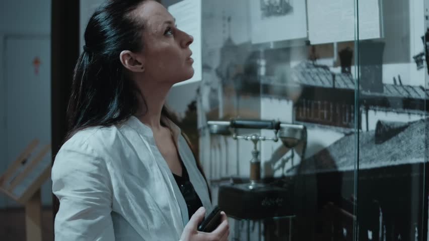 Thoughtful young Caucasian woman looking at exhibition at museum. In background, retro objects of Soviet Union times and pictures under glass. 2023, Museum of History, Chisinau, Moldova