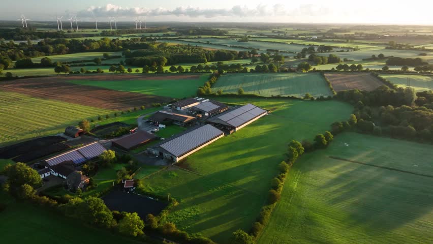 Camera panning from left to right from modern agriculture livestock farm with photovoltaic panels on the roofs of barn to foggy landcape with fields, medows in the morning haze at sunrise. 