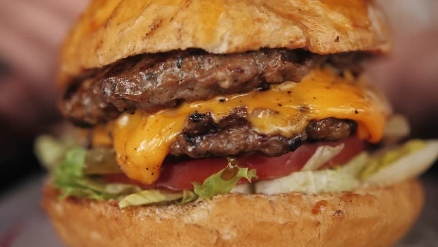 Grilled beef burger with melted cheese and fresh vegetables on a table. Fast food Unhealthy diet.