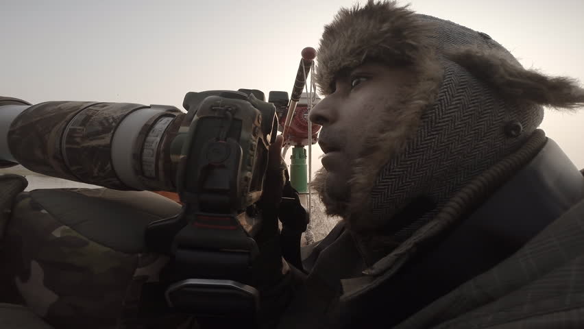 A bird and wildlife photographer clicking photos from a boat with a Canon DSLR camera and telephoto lens