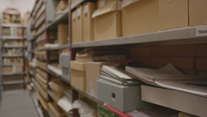 Pan over aisle of archive with cardboard boxes and files