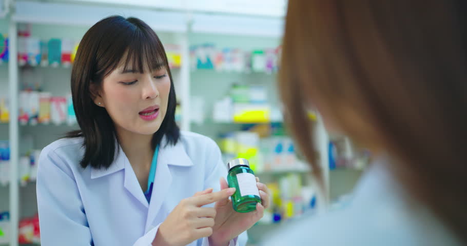 Young asian pharmacist talking with customer at pharmacy counter. She tells customers about drug information at the pharmacy.