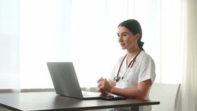 Attractive young female doctor making an online video call and consulting a patient on a laptop. Video conference of a medical assistant. Webcam view. Telemedicine pandemic concept.