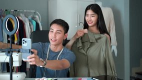 Professional Asian male and female fashion designer is making a video live streaming on social network to show their works. Happy Asian young couple enjoy making a live video.