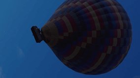 Vertical video. View from below of a multicolored hot air balloon with people in the basket. It's igniting from the inside with flames, and it continues to rise higher and higher.