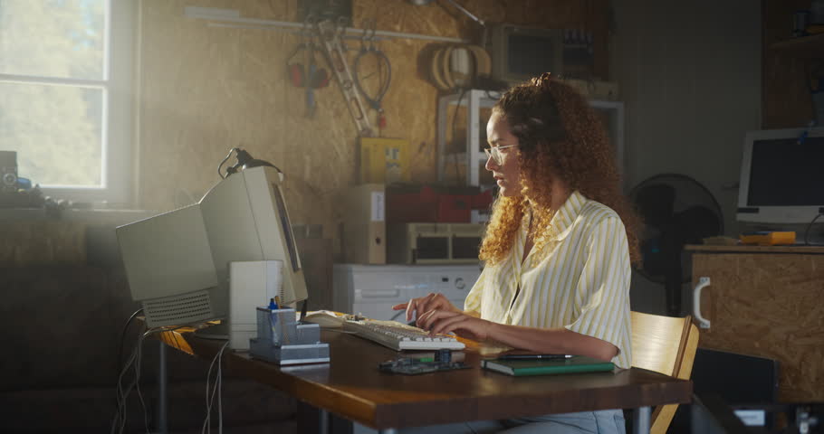 Hispanic Female Software Engineer Programming On Old Desktop Computer In Retro Garage, Looking At Camera And Smiling. Woman Starting an Innovative Startup Company In Nineties. Nostalgia Concept. Royalty-Free Stock Footage #1109860295