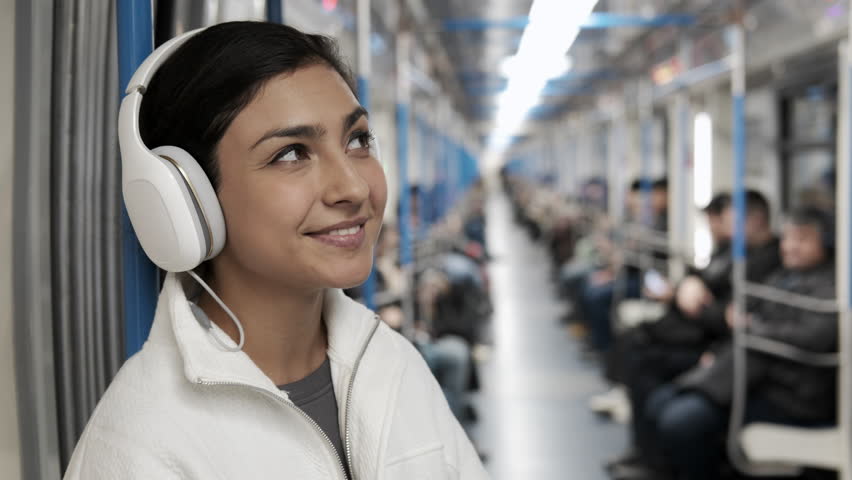 Pretty girl looking at camera and smiling. Portrait of young happy woman in subway. Beautiful stylish girl with headphones. Metro concept. Listening and enjoying music. Female joyful student. 4K Royalty-Free Stock Footage #1109868849