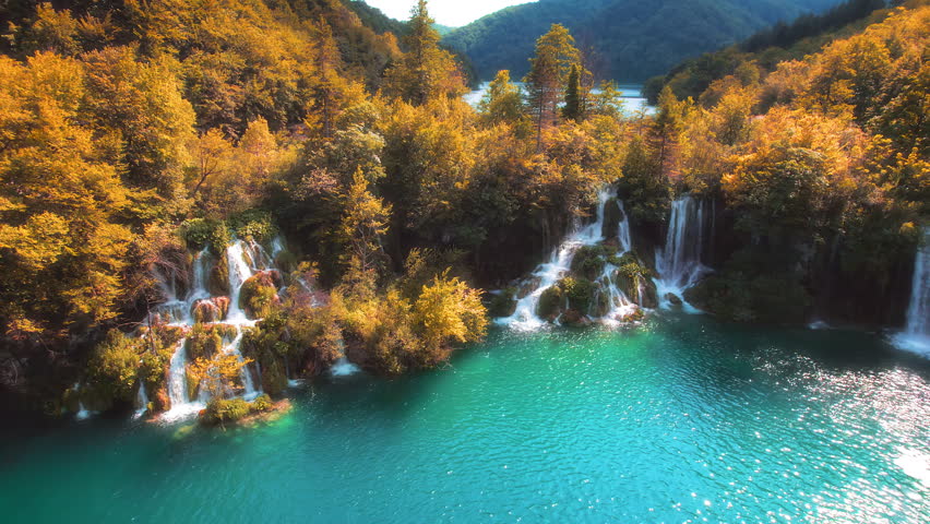 Golden autumn forest and mountain lake with amazing waterfalls. Clear emerald green water. Sunny weather quickly changes to dark.