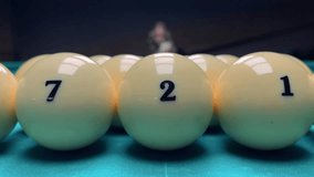 4K video. Woman in blurred black dress aims at pyramid of white billiard balls on blue pool table in dark club. Ball with number. Camera movement. Concept of gambling, sports, retro vibe, betting. Pub