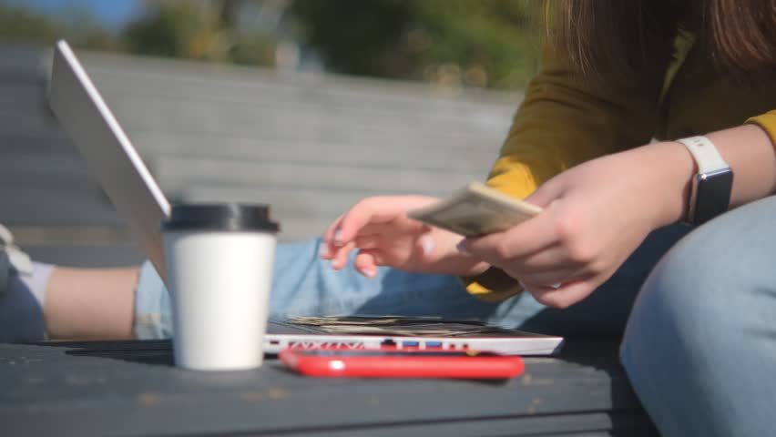Caucasian woman counts dollars, typing on a keyboard laptop, while sitting on the outdoor in the early morning time. 4K