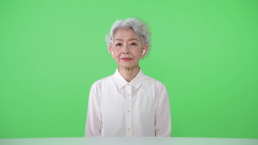 Elderly Asian woman talking to camera. Green background for chroma key composition. Royalty-Free Stock Footage #1109875081