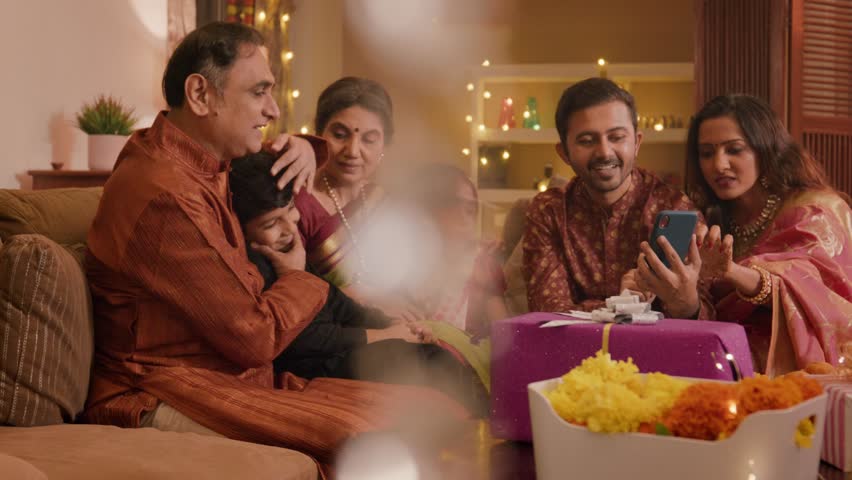 Happy Hindu ethnic Indian family members in traditional wear sitting indoors together interacting with each other while shopping online using a mobile phone or smartphone during Diwali festival season | Shutterstock HD Video #1109881935