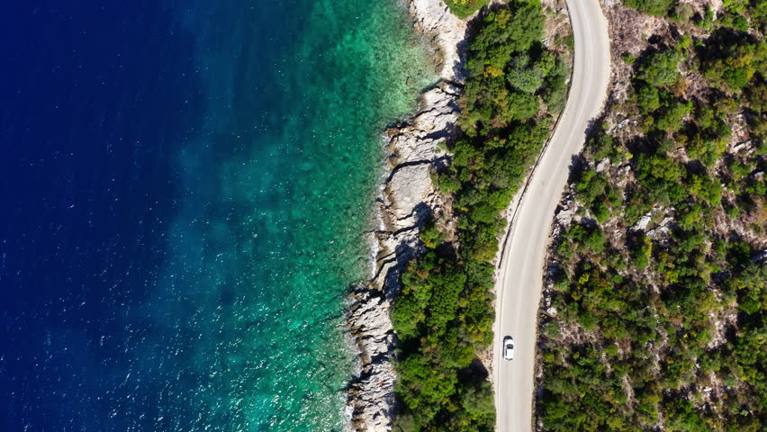 Drone camera tilting following the car moving by the sea curved road near a tranquille waves on the Greek coast on Cephalonia island. Transportation, nature 4K aerial video concept. Royalty-Free Stock Footage #1109883705