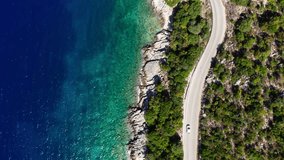 Drone camera tilting following the car moving by the sea curved road near a tranquille waves on the Greek coast on Cephalonia island. Transportation, nature 4K aerial video concept.