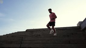A male athletic instructor runs down the stairs in running shoes and sportswear for outdoor training. Athlete intensive workout warm-up in the city. Slow motion video.
