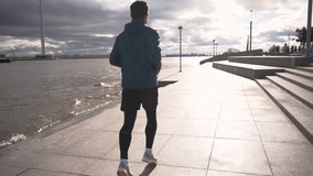 A young man is preparing for a triathlon, running alone on the street in the weather. Running rear view male fitness workout every day for mental and psychological health. Slow motion video.