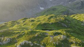 The drone video captures a breathtaking view of a wide green valley amidst low mountains, with a winding road and a small european village. The sky is covered with clouds, and the drone flies through.