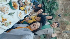 Group of joyful friends posing together for camera at table with food and drinks, video calling or taking selfie on backyard dinner party. Vertical format footage - Powered by Shutterstock - Get 15% off with code: PIKWIZARD15