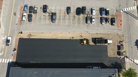 Time lapse drone footage of a work crew applying asphalt to a parking lot, looking down from above. Static shot.