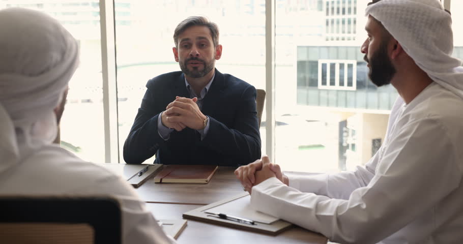 Positive middle-aged Portuguese businessman hold negotiation with Muslim partners sit at desk in modern conference room reach agreement feel satisfied with successful meeting, shake hands look happy Royalty-Free Stock Footage #1109893483