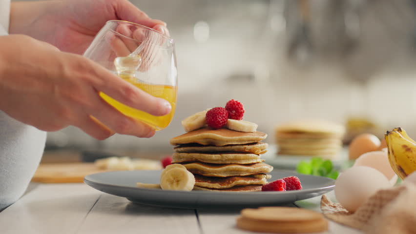 The master chef pours honey on pancakes with berries. Cameras young parent pours yellow honey on pancakes with fruits applies new mixing of different fruits and berries, sweet food Royalty-Free Stock Footage #1109894523