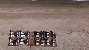 Cafe or restaurant chairs and tables on a wooden platform near the sea. Aerial video empty beach view down.
