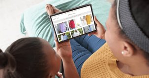 African american mother and daughter using tablet, online shopping for clothes, slow motion. Retail business, sale, communication and digital interface digitally generated video.