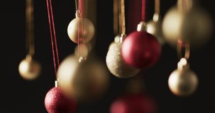 Video of gold and red christmas baubles decorations with copy space on black background. Christmas, decoration, tradition and celebration concept.