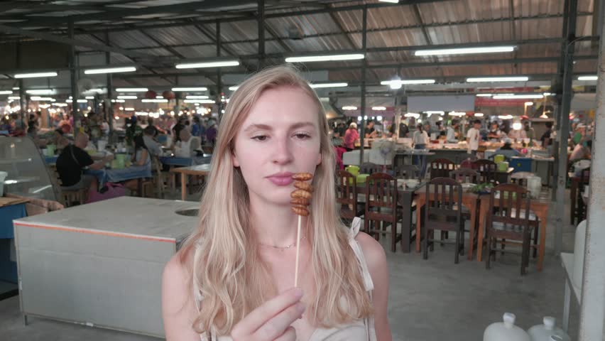 Caucasian woman eats fried insects at a night market in Thailand. Close-up.