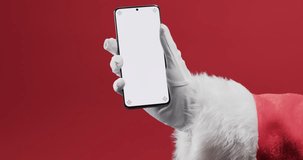 Video of santa claus holding smartphone with copy space on red background. Christmas, decorations, tradition and celebration concept.