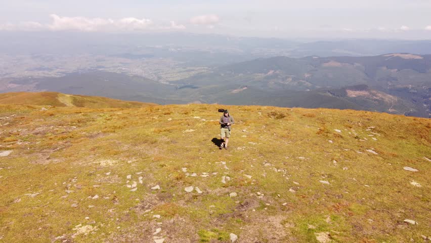 Drone pilot man with remote control outdoors on top of mountains. A professional aerial photographer and drone operator manages the flight and filming. 