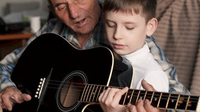 Grandfather holding grandson's hand and teaching him to play guitar on sofa at home. - Powered by Shutterstock - Get 15% off with code: PIKWIZARD15