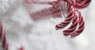 Vertical video of christmas candy canes in glass jar and copy space on snow background. Christmas, dessert, baking, decorations, tradition and celebration concept.